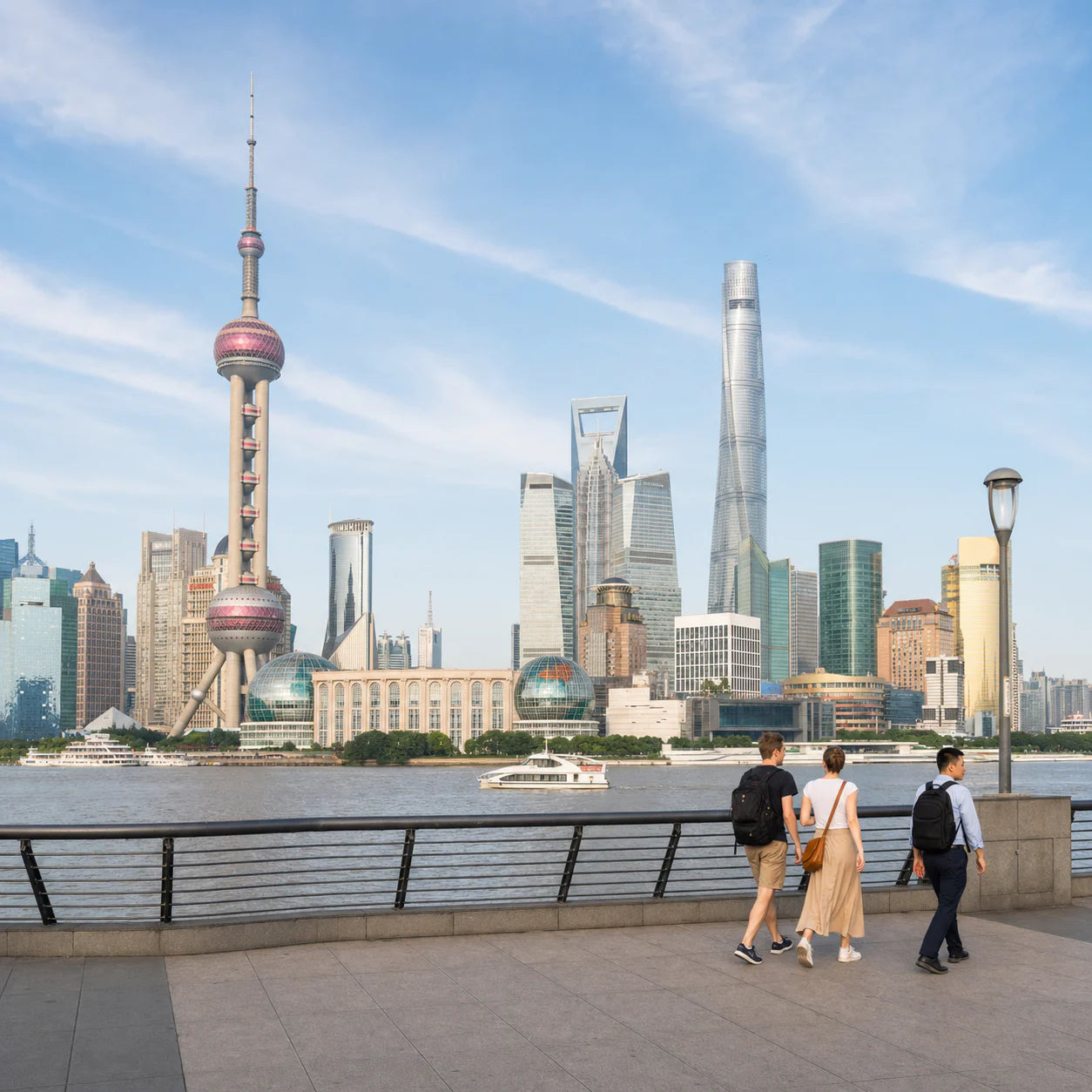 Travelers walking along the Bund with the Oriental Pearl Tower and Lujiazui skyline across the Huangpu River